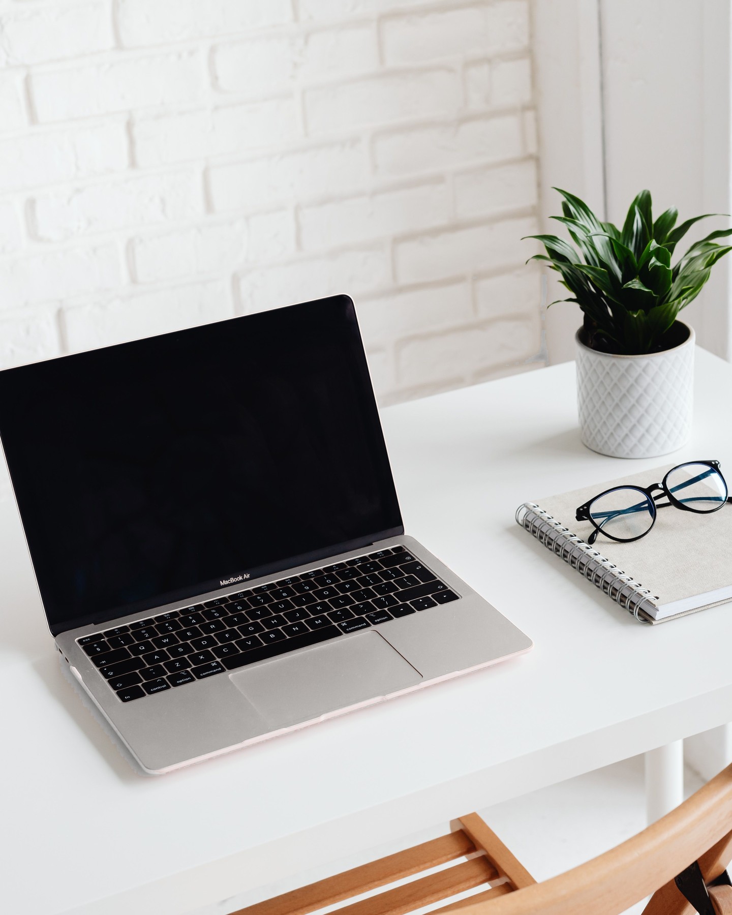Bright organized workspace with laptop, notebook, glasses, and a green plant.